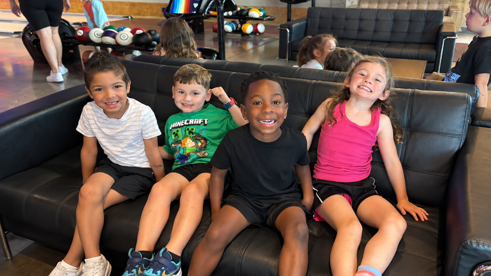 Four school-age children smiling together on a couch during a bowling alley field trip