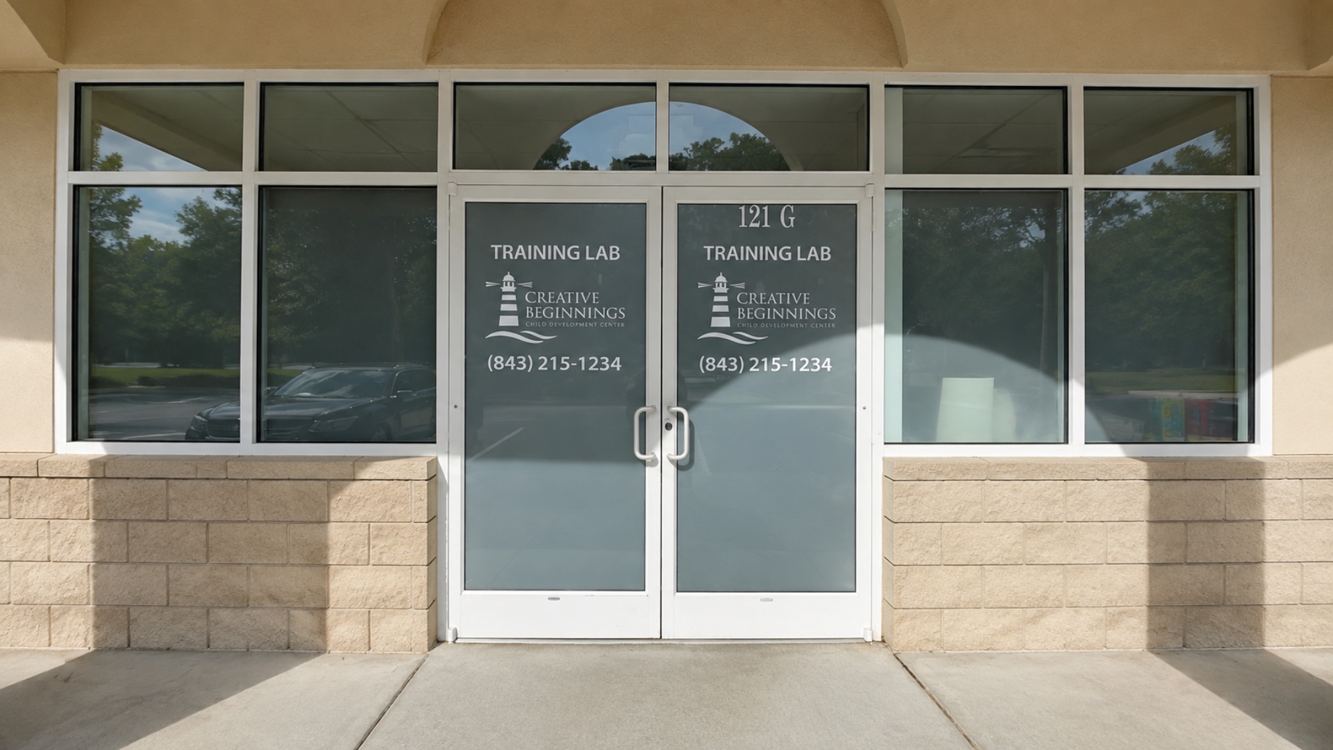 Glass entrance doors of the Creative Beginnings Training Lab, etched with the lighthouse logo, suite number 121 G and the phone number 843-215-1234