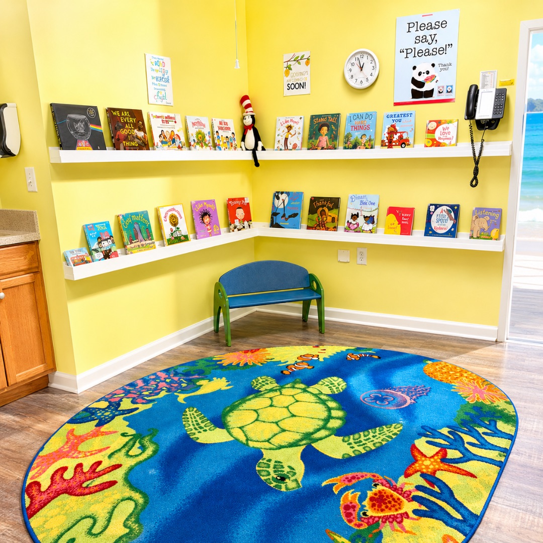 Sunny yellow library nook with picture books lined along white shelves, a small blue bench and an oval sea-turtle reading rug