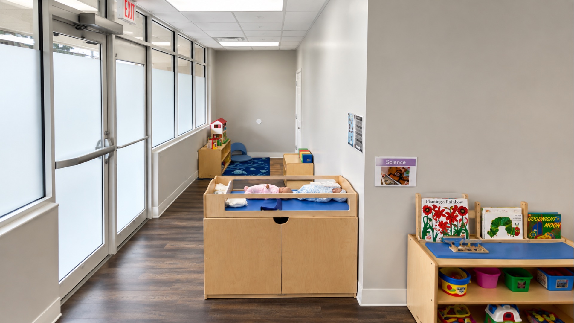 Infant training room with a wooden changing station holding two practice dolls, a science learning area sign and a shelf of board books
