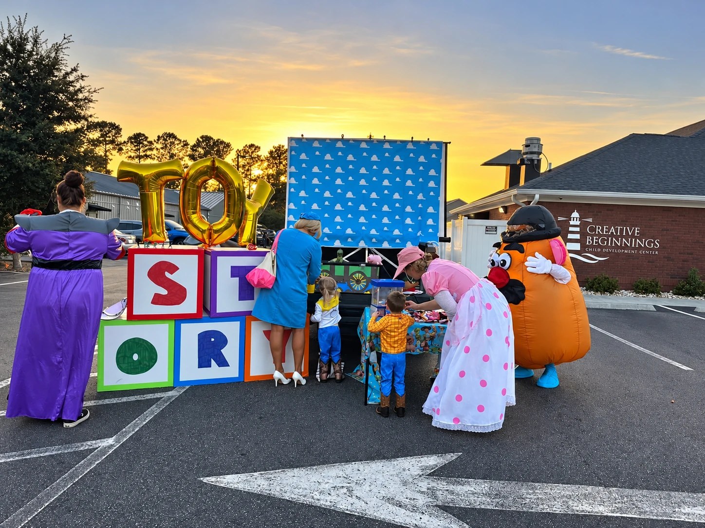 Teachers in Toy Story costumes running a kids' game table outside a Creative Beginnings campus at sunset