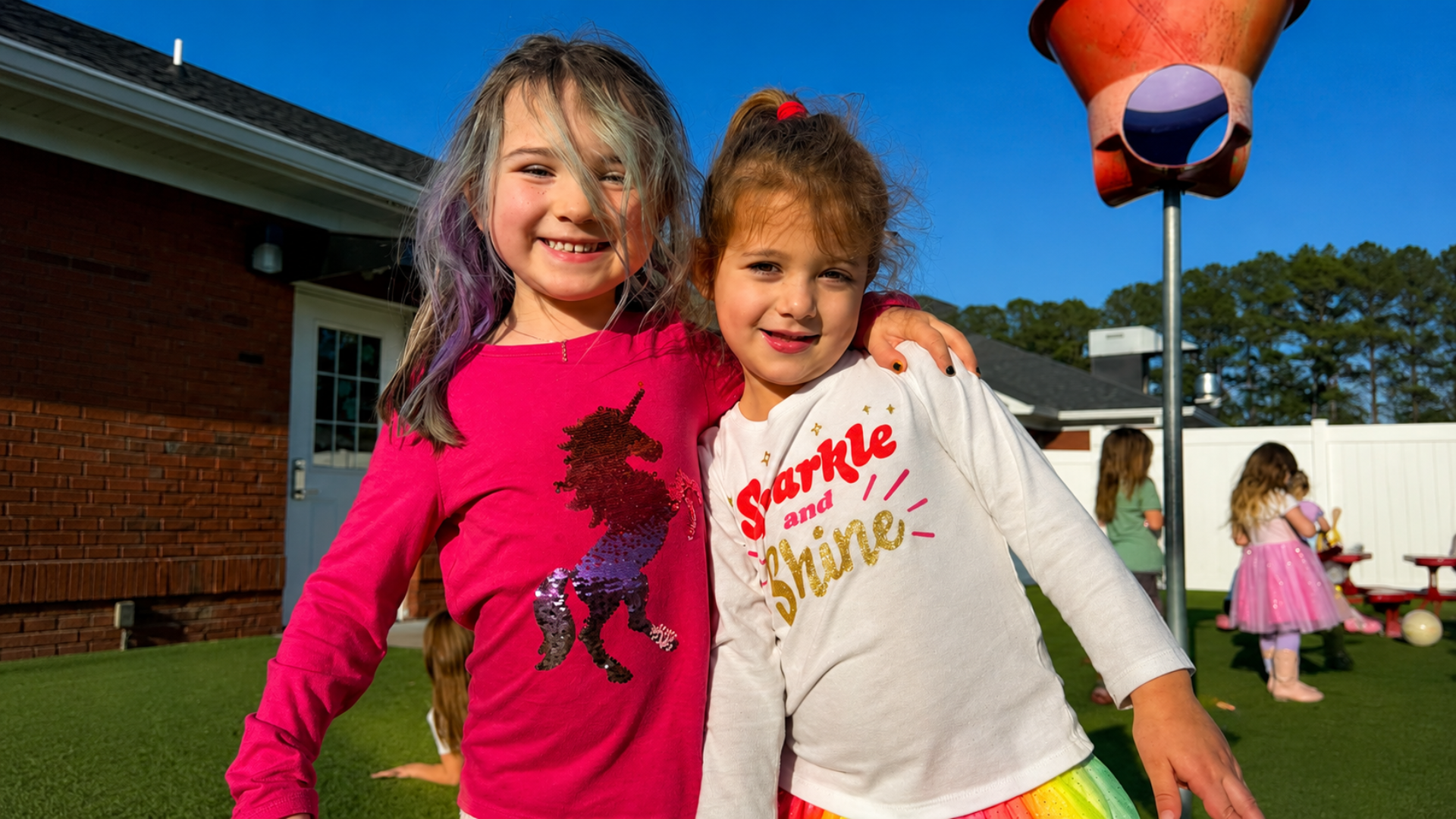 Two school-age girls hugging and smiling outside on the playground on a sunny afternoon